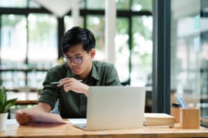 Boy studying with notes and laptop.